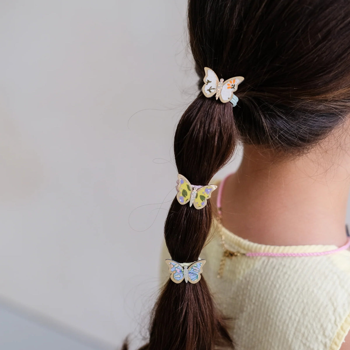 Butterfly hair clips on a person's ponytail against a neutral background