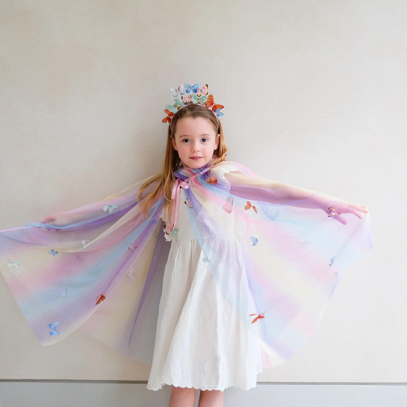 Young girl with butterfly-themed headband,cape and wand against a blue background
