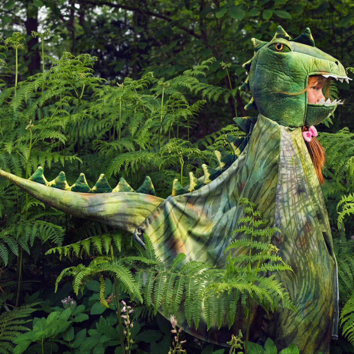 Child in a green dinosaur costume standing in a forest