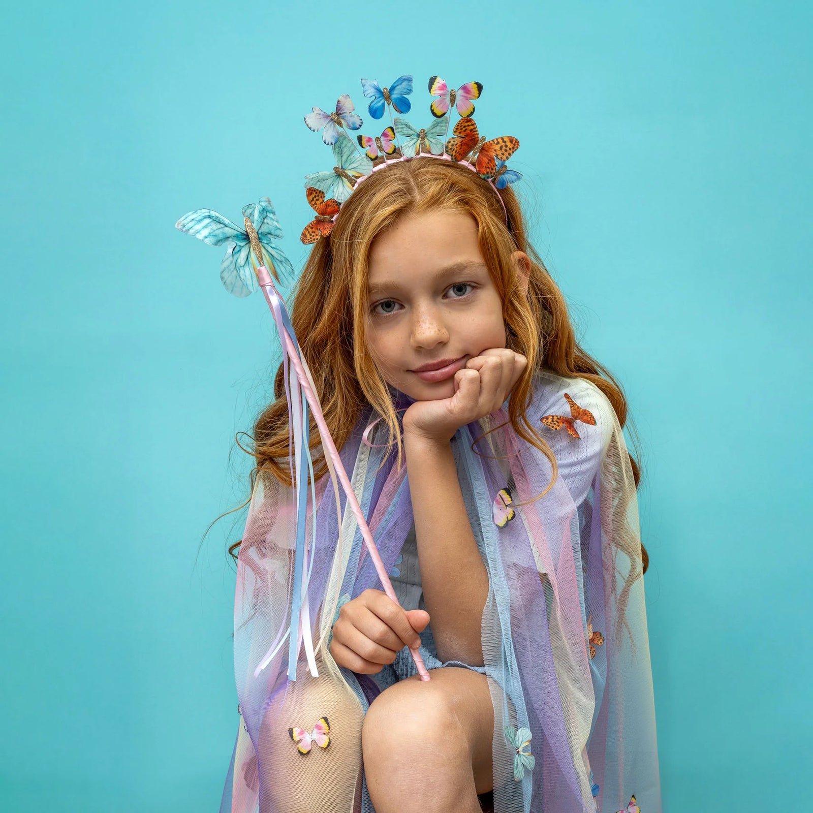 Young girl with butterfly-themed headband,cape and wand against a blue background