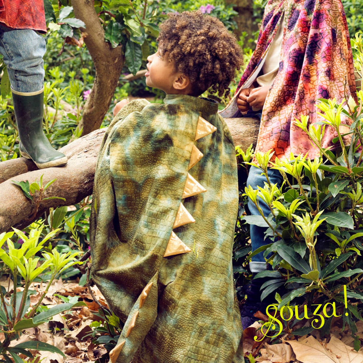 Child wearing a green dinosaur costume in a garden setting with 'gouza!' branding.