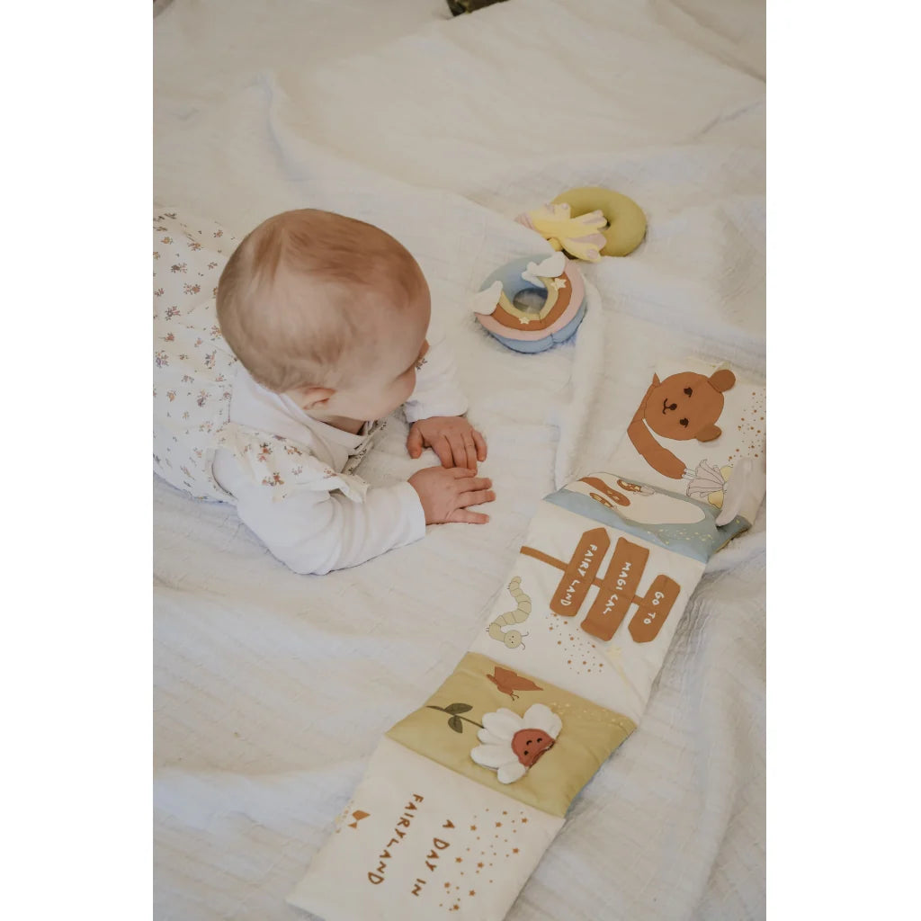 Baby lying on a bed with a soft book and toys