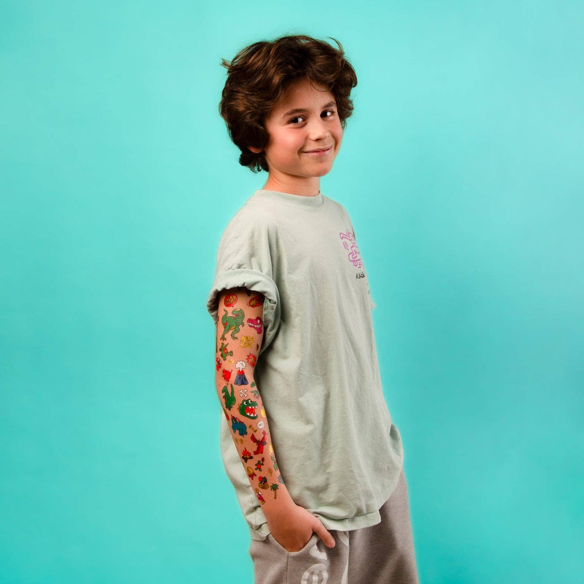 Child with tattoos on arm wearing a gray t-shirt against a blue background