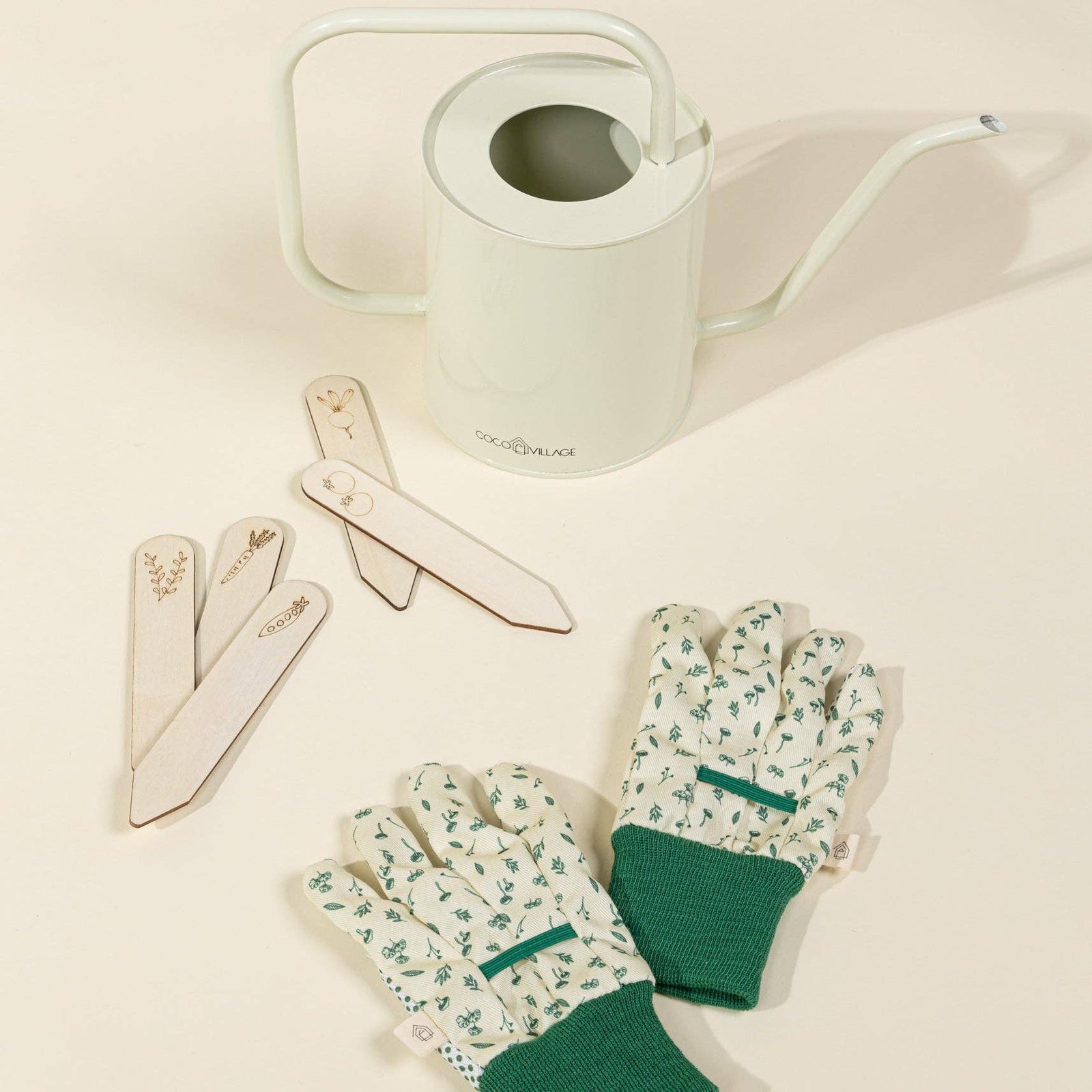 Gardening tools including a watering can, trowel, and fork on a light beige background.